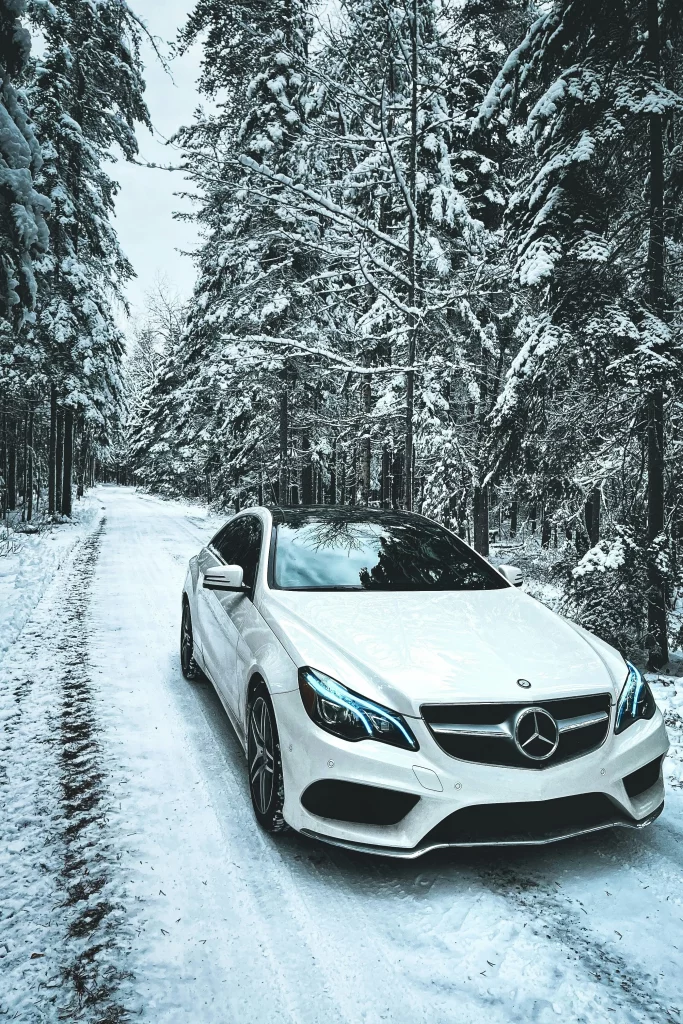 Weißer Mercedes mit Motorschaden im verschneiten Wald auf winterlicher Straße