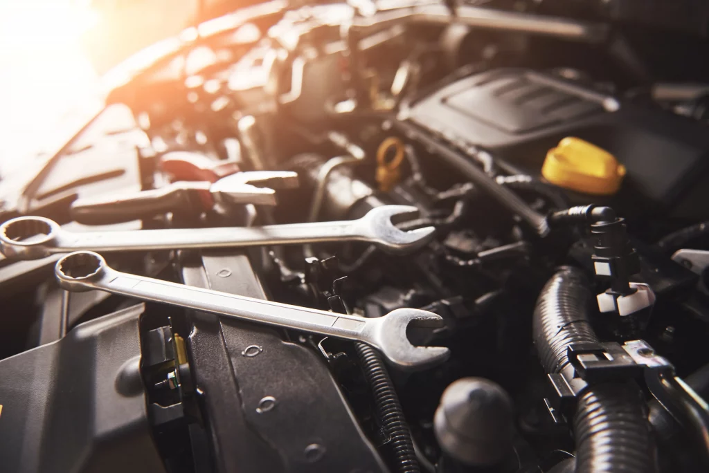 Mechaniker überprüft den Motor eines kaputten Fahrzeugs mit Werkzeugen auf dem Motorblock in einer Autowerkstatt